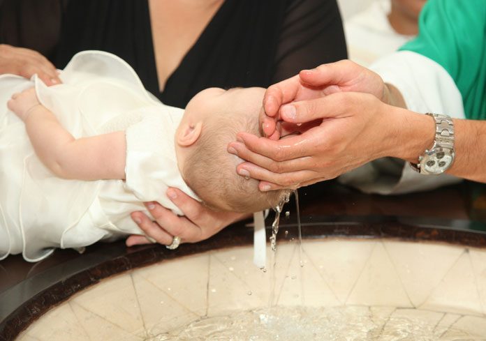 Baby wird über das Taufbecken gehalten und getauft